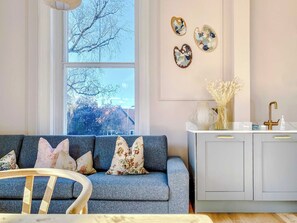 A living room with a sofa, a coffee table, and a window with a view of trees.