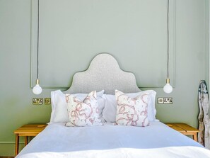A neatly made bed with white bedding and decorative pillows, a wooden nightstand, and a wall-mounted light fixture.