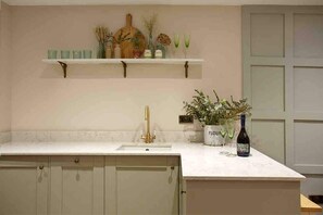 A kitchen with a white countertop, a gold faucet, and a wine bottle.