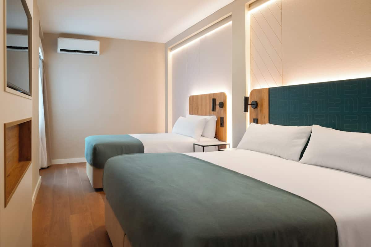 A hotel room with two beds, a wooden headboard, a wall-mounted air conditioner, and a bedside table.