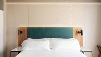 Una habitación de hotel moderna con una cama grande, cabecera de madera con patrón geométrico y dos mesitas de noche con lámparas.