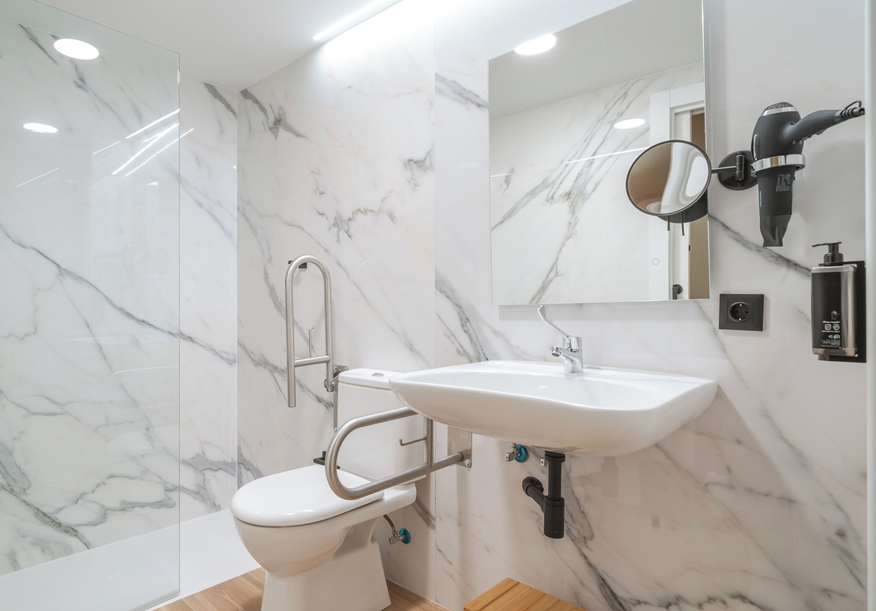 Un baño moderno con pared de mármol, lavamanos blanco, secador de pelo de mano y espejo.