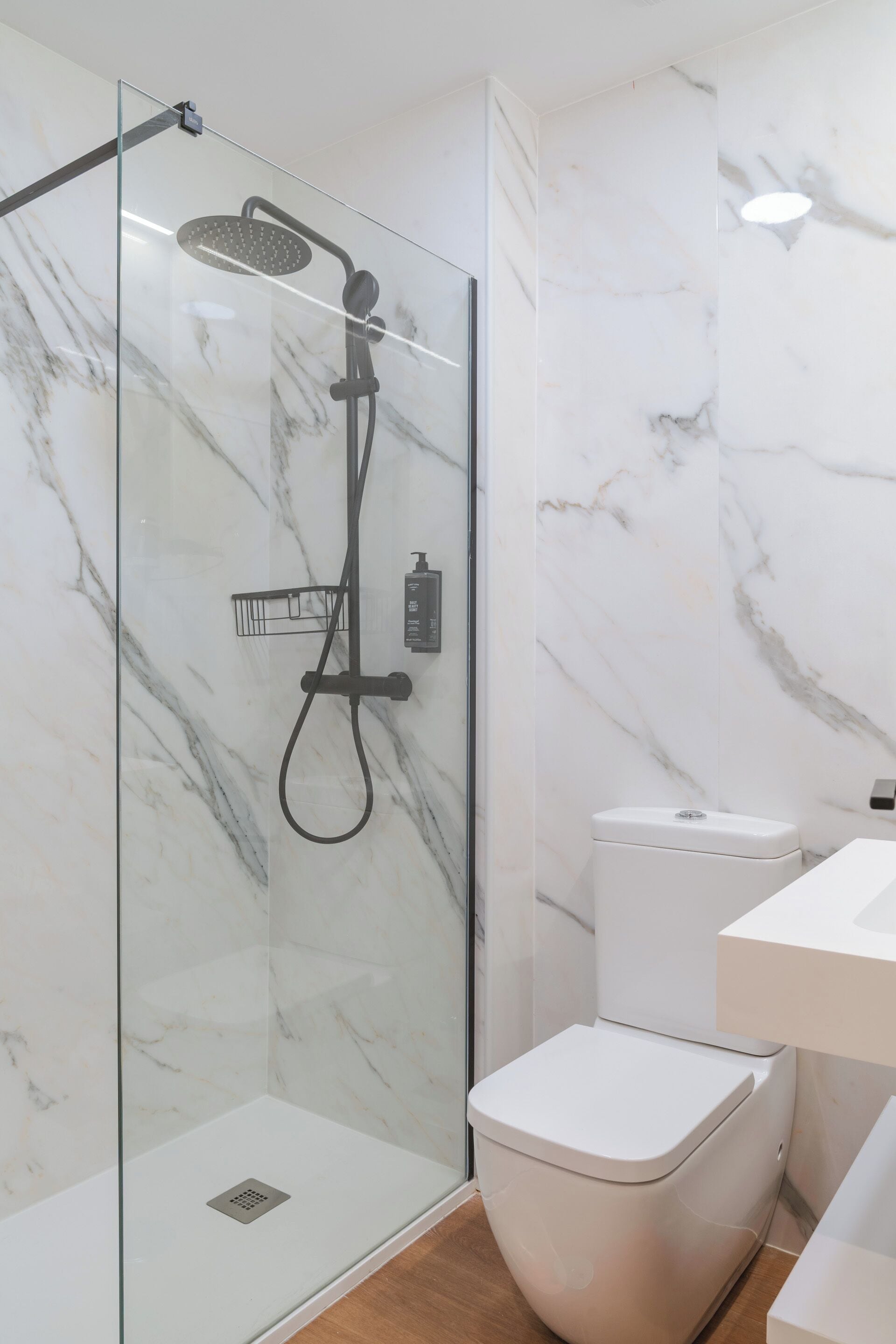 A modern bathroom with a glass-enclosed shower, a white toilet, and a marble wall.