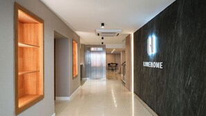 Un pasillo moderno de hotel con suelo pulido, estanterías de madera, un ascensor y una pared de mármol con el nombre del hotel.