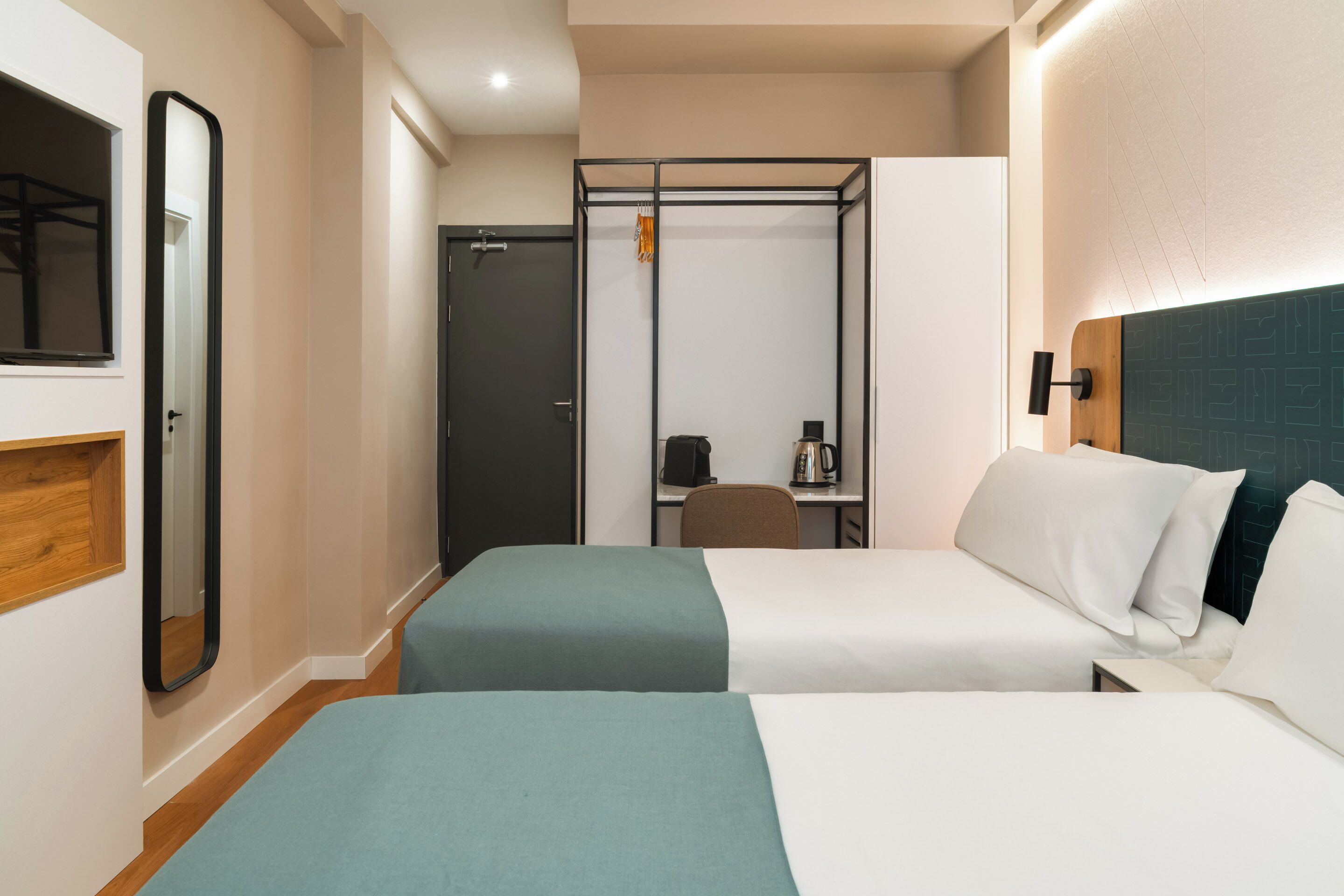 A hotel room with two beds, a desk, a chair, a coffee maker, and a wardrobe.