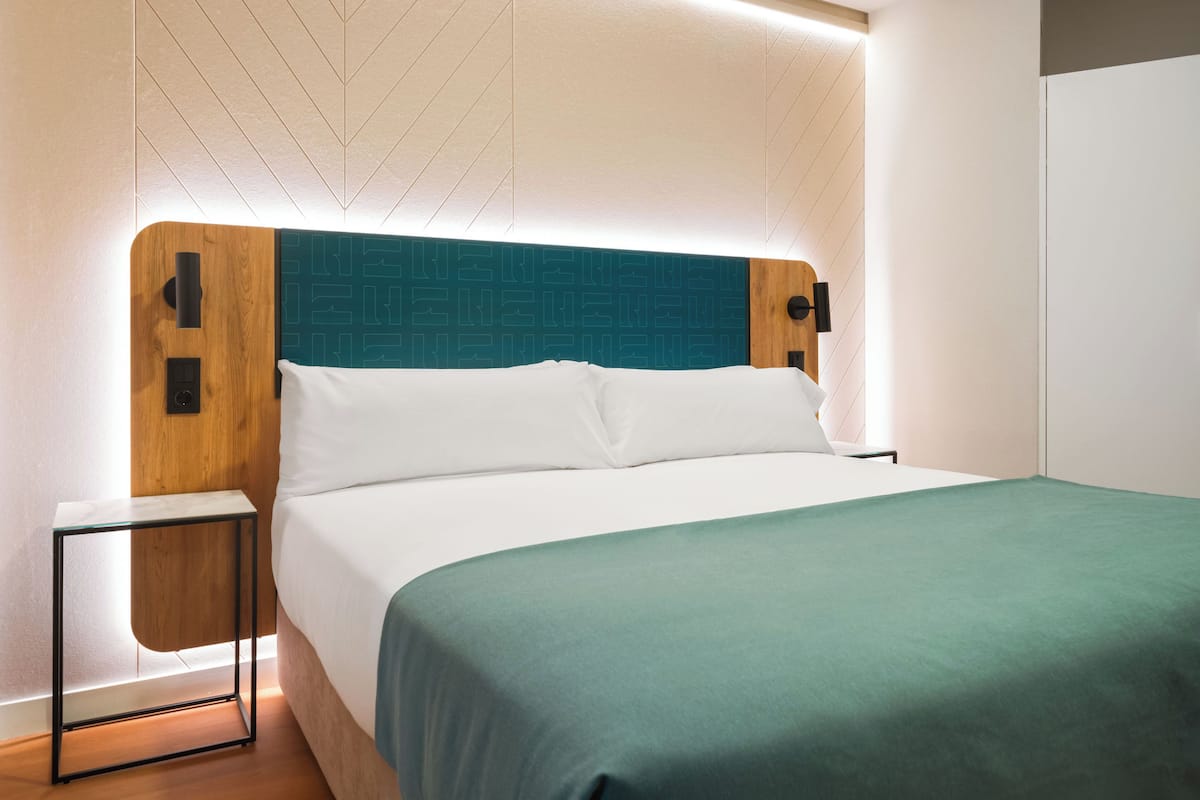 A modern bedroom with a bed, a nightstand, and a wall-mounted light fixture.