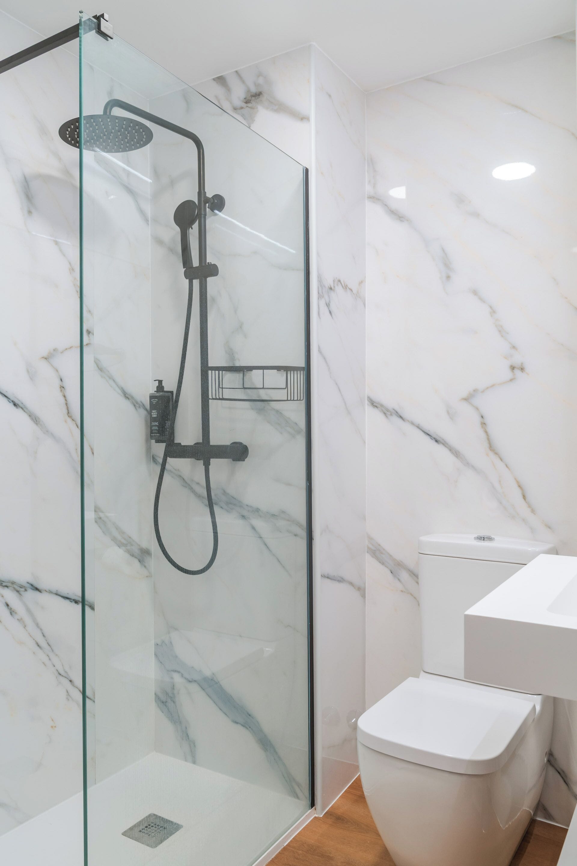 A modern bathroom with a glass-enclosed shower, white marble walls, and a white toilet.