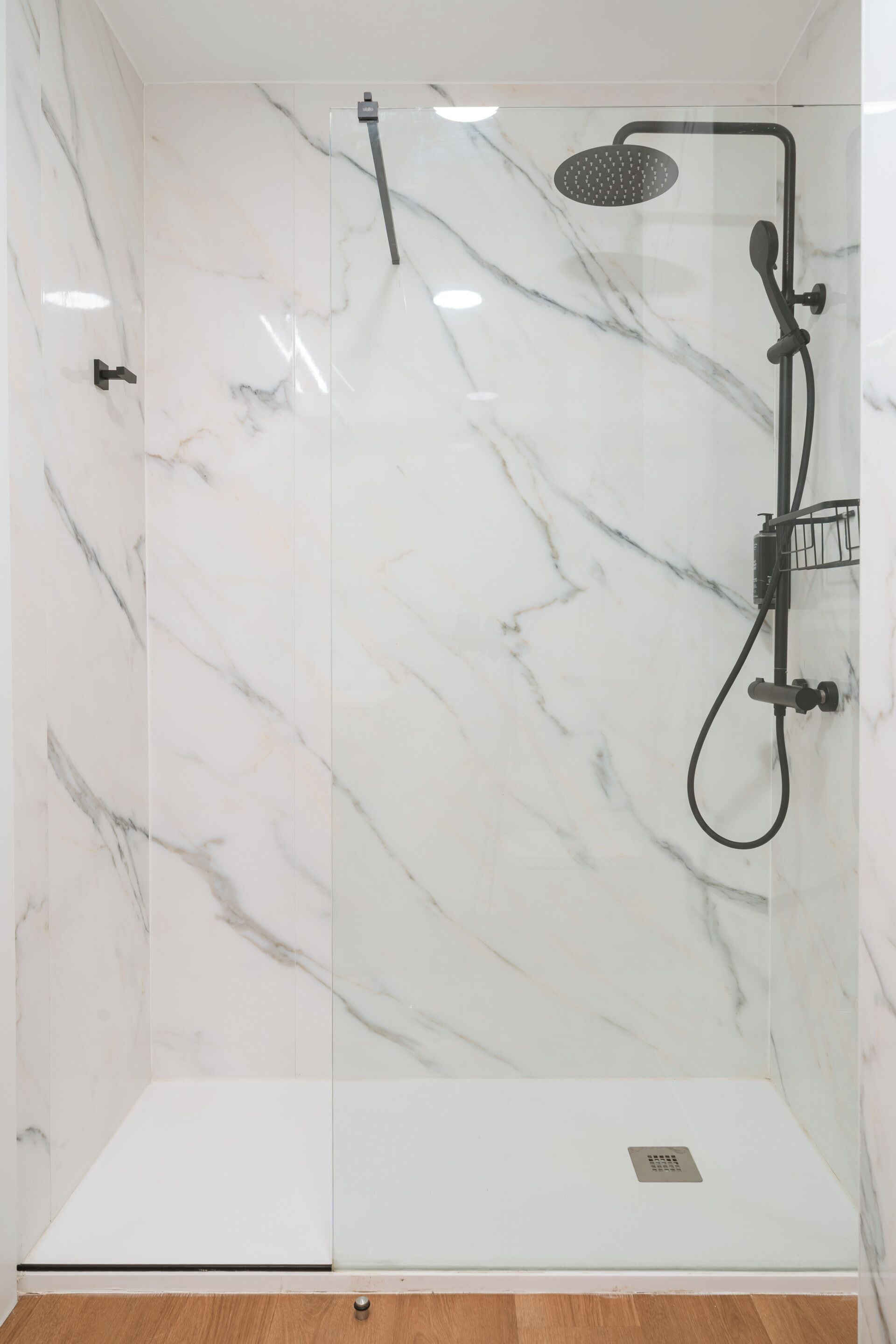 Une douche fermée par des parois en verre, dotée d’un pommeau de douche à main et d’un robinet mural.