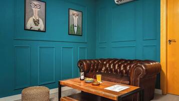 Une pièce aux murs de couleur turquoise, avec un canapé en cuir, une table basse en bois sur laquelle se trouvent une bouteille et un verre, et deux œuvres d’art encadrées.