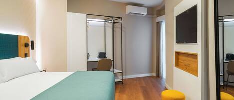 Una habitación de hotel con una cama, un escritorio, una silla, un taburete, un equipo de aire acondicionado y un espejo.