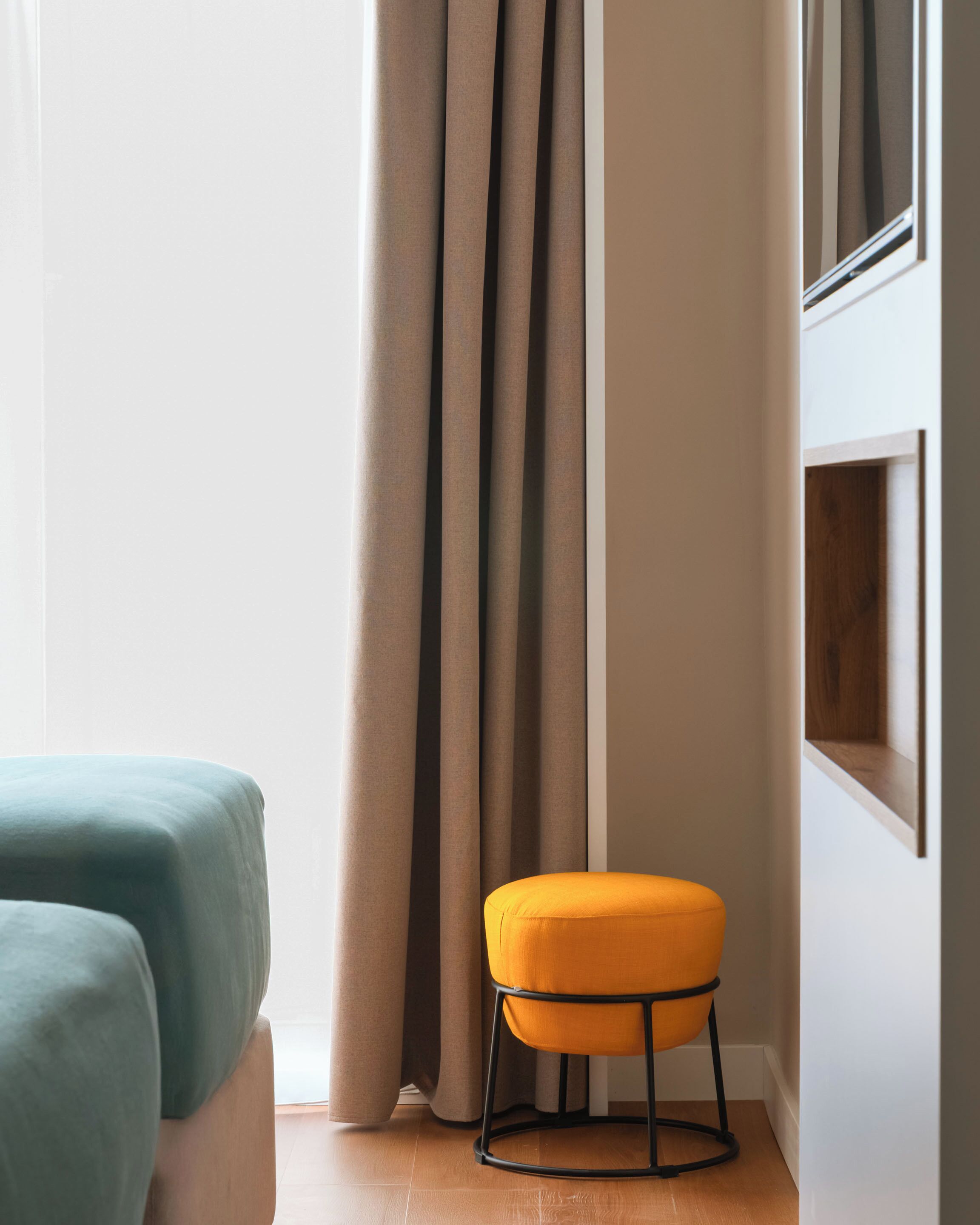 A room with a bed, a small stool, and a window with curtains.