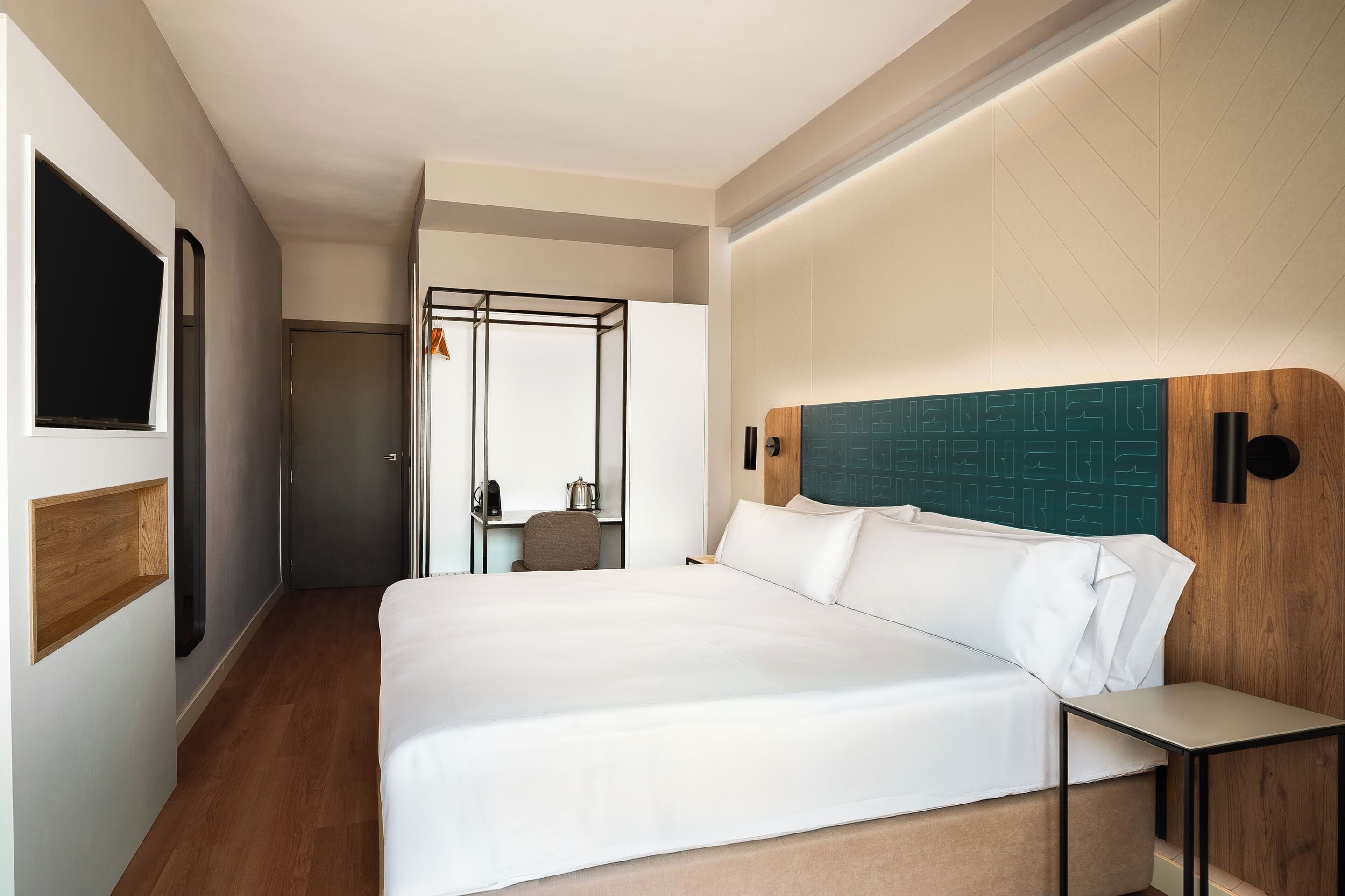 A hotel room with a large bed, a bedside table, a wooden headboard, and a view of a hallway.
