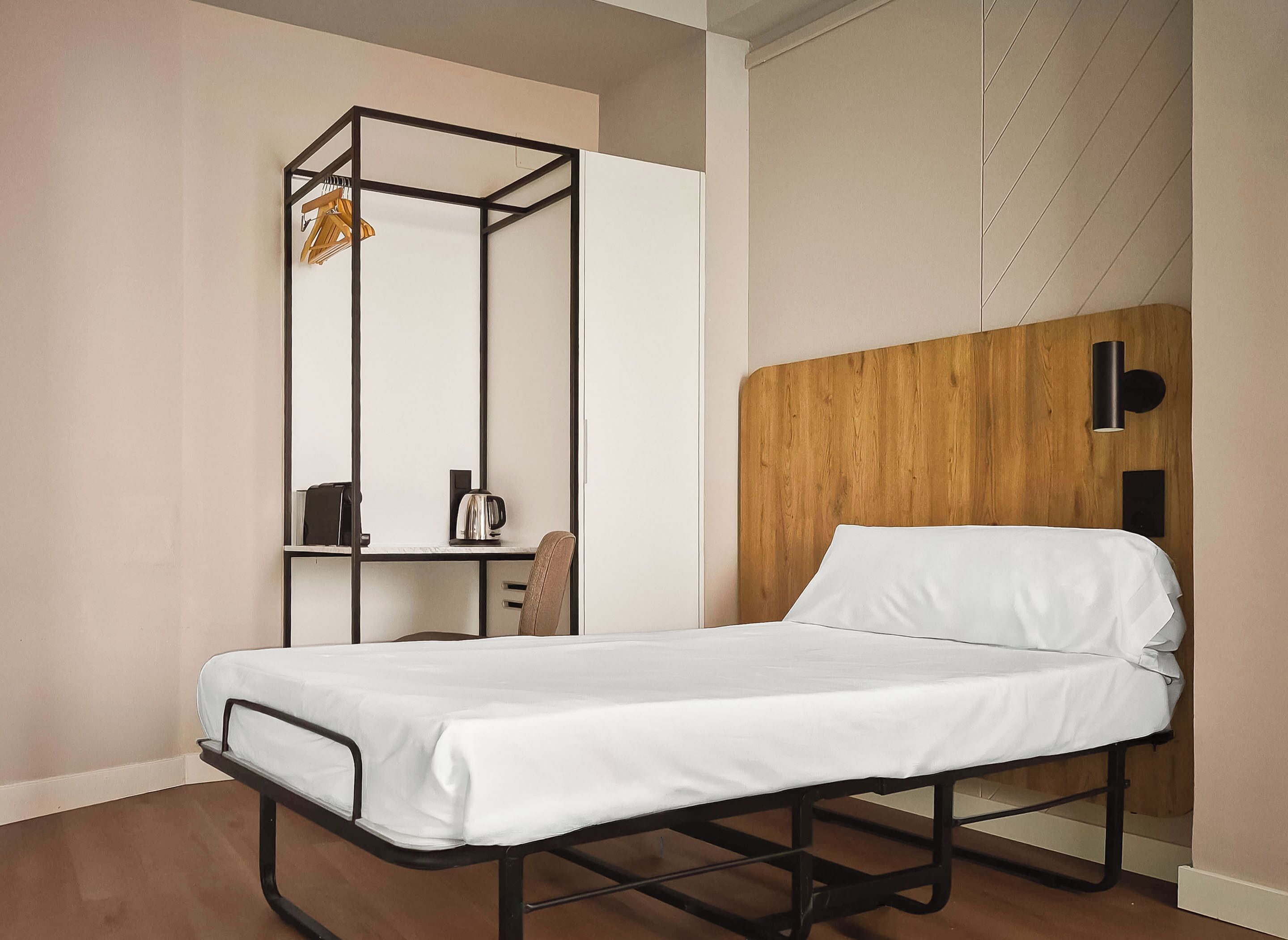 A single bed with a wooden headboard, a metal-framed desk with a chair, and a hanging light fixture.