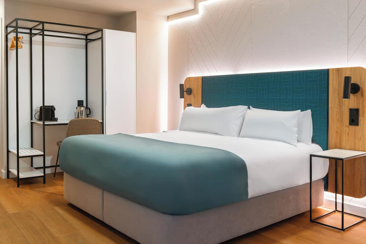 A modern hotel room with a large bed, a desk, and a wardrobe.