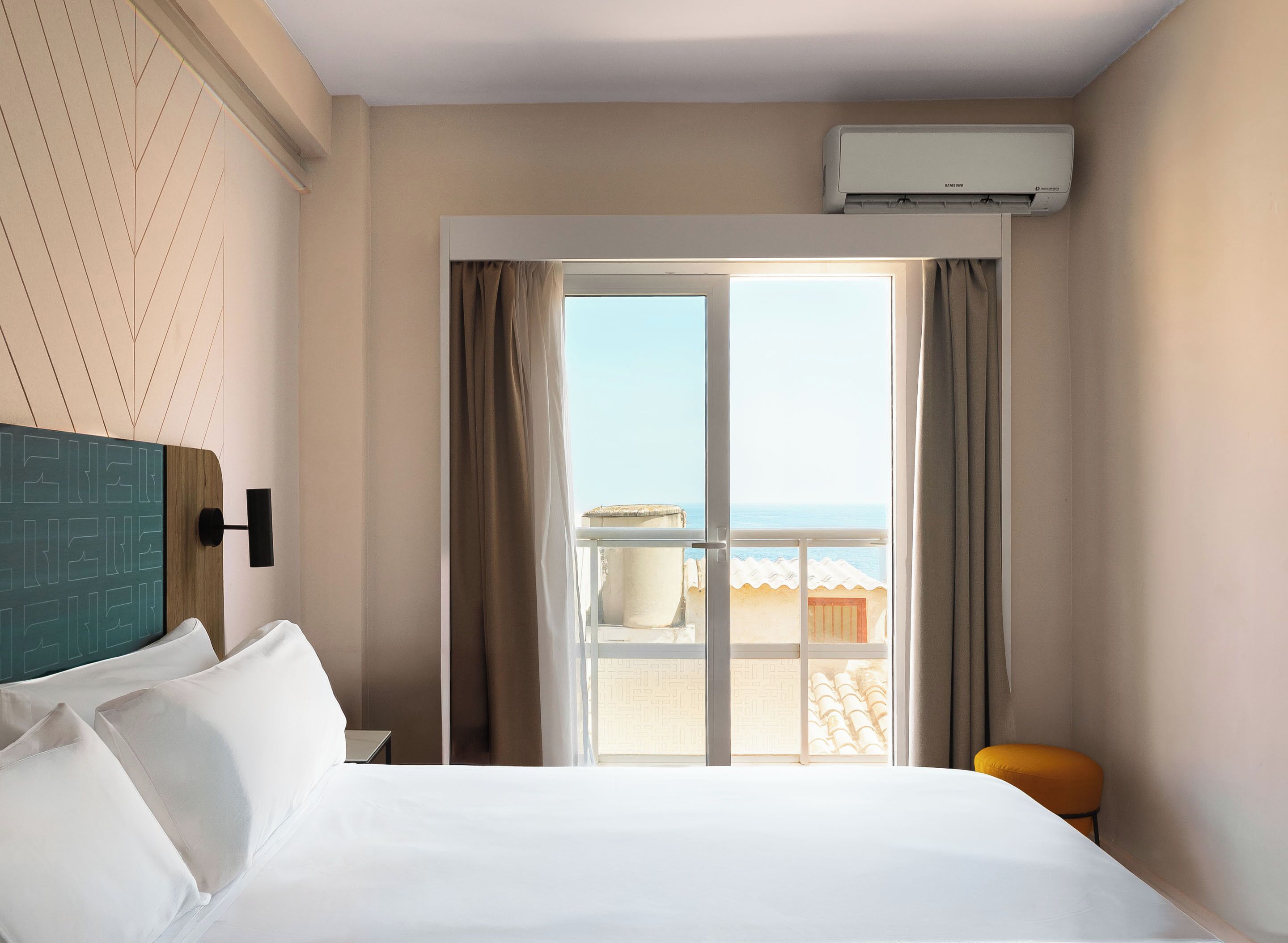 A hotel room with a bed, a view of the sea, and an air conditioning unit.