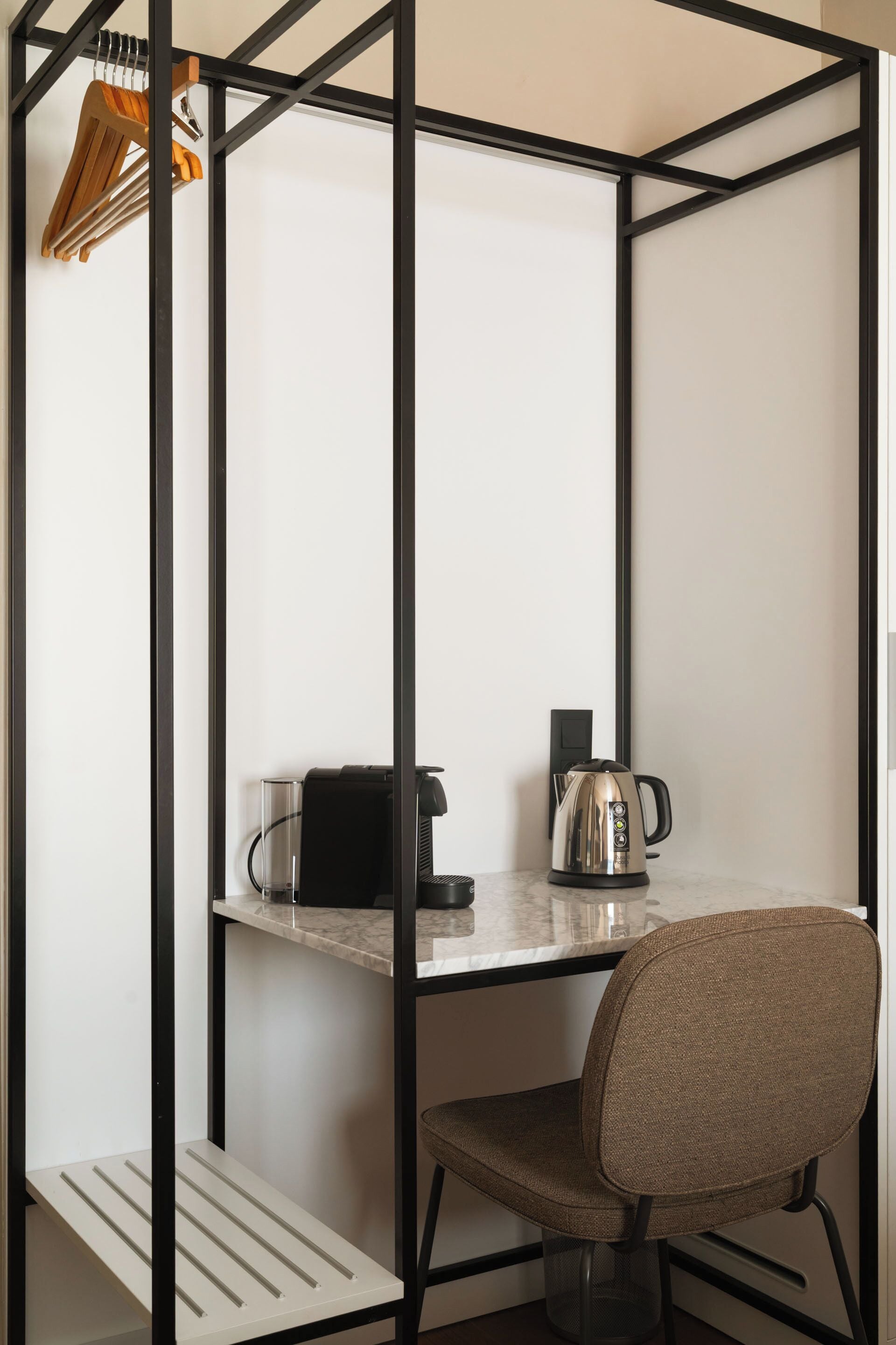 A compact room with a desk, a chair, a kettle, and a coffee maker.