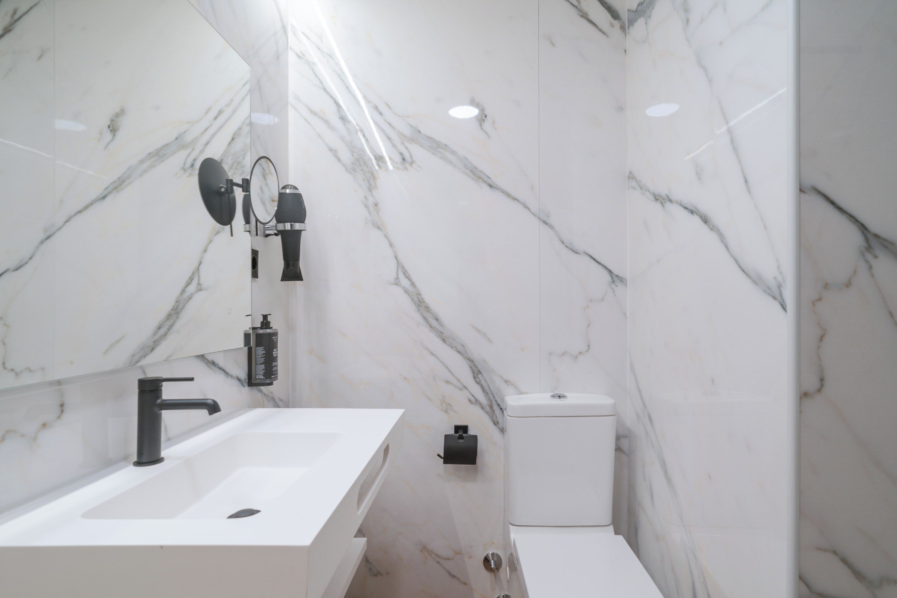 A modern bathroom with a white sink, black faucet, and marble walls.