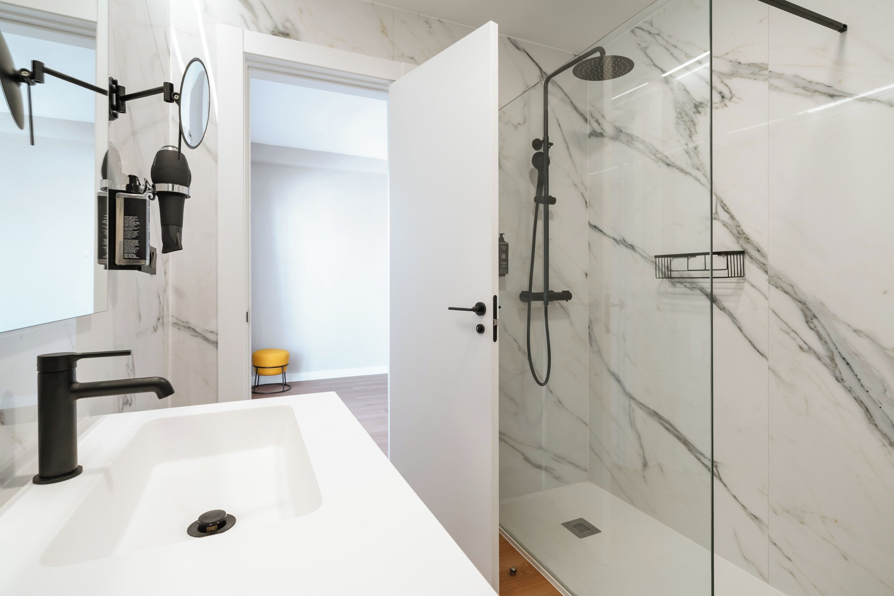 A modern bathroom with a white sink, black faucet, and a glass-enclosed shower with a marble wall.