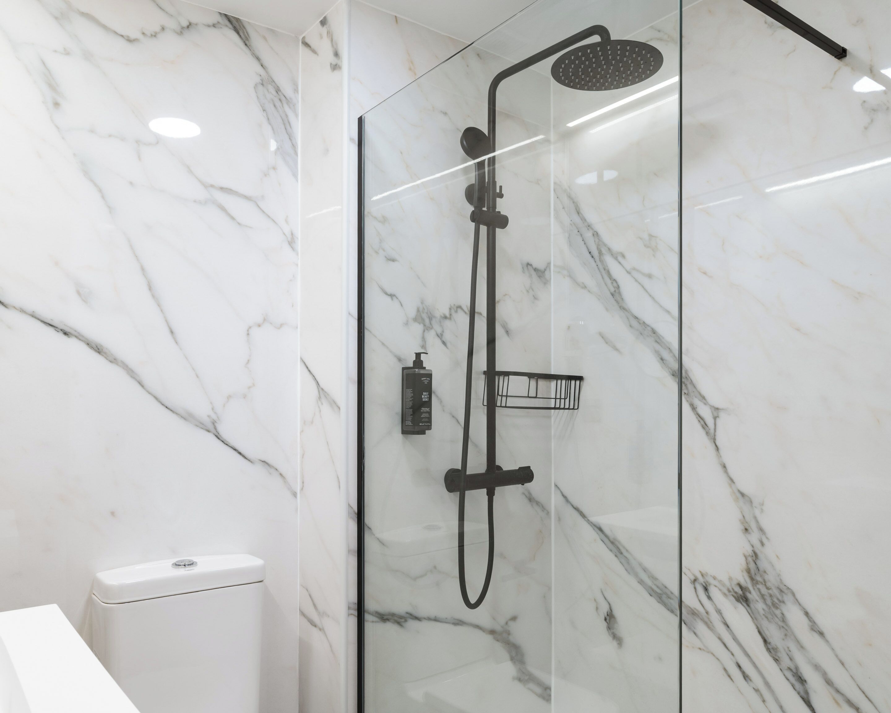 A modern bathroom with a glass-enclosed shower, marble walls, and a white toilet.