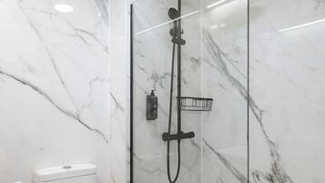 A modern bathroom with a glass-enclosed shower, marble walls, and a white toilet.