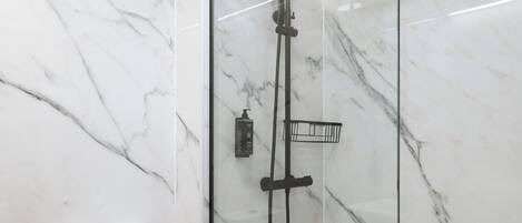 A modern bathroom with a glass-enclosed shower, marble walls, and a white toilet.