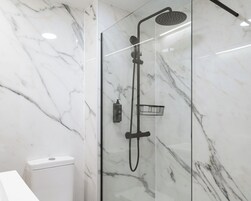 A modern bathroom with a glass-enclosed shower, marble walls, and a white toilet.