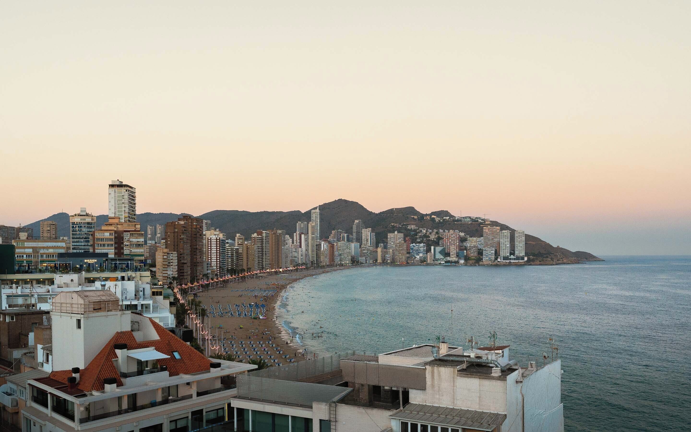 A coastal cityscape with a beach, high-rise buildings, and a mountain in the background.
