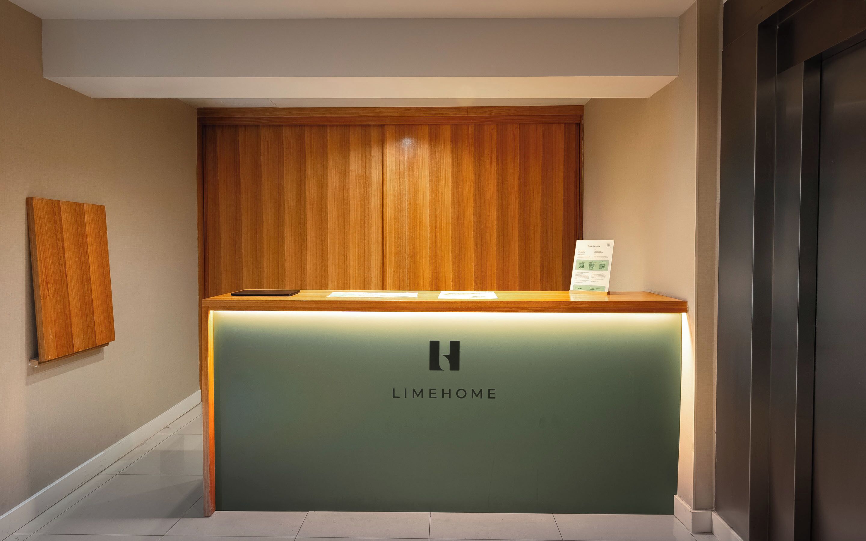 A reception desk with a wooden panel and a green counter, featuring the logo 'LIMEHOME'.