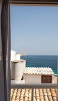 Une vue sur la côte depuis un balcon, avec un ciel dégagé, un voilier au loin et une côte rocheuse.