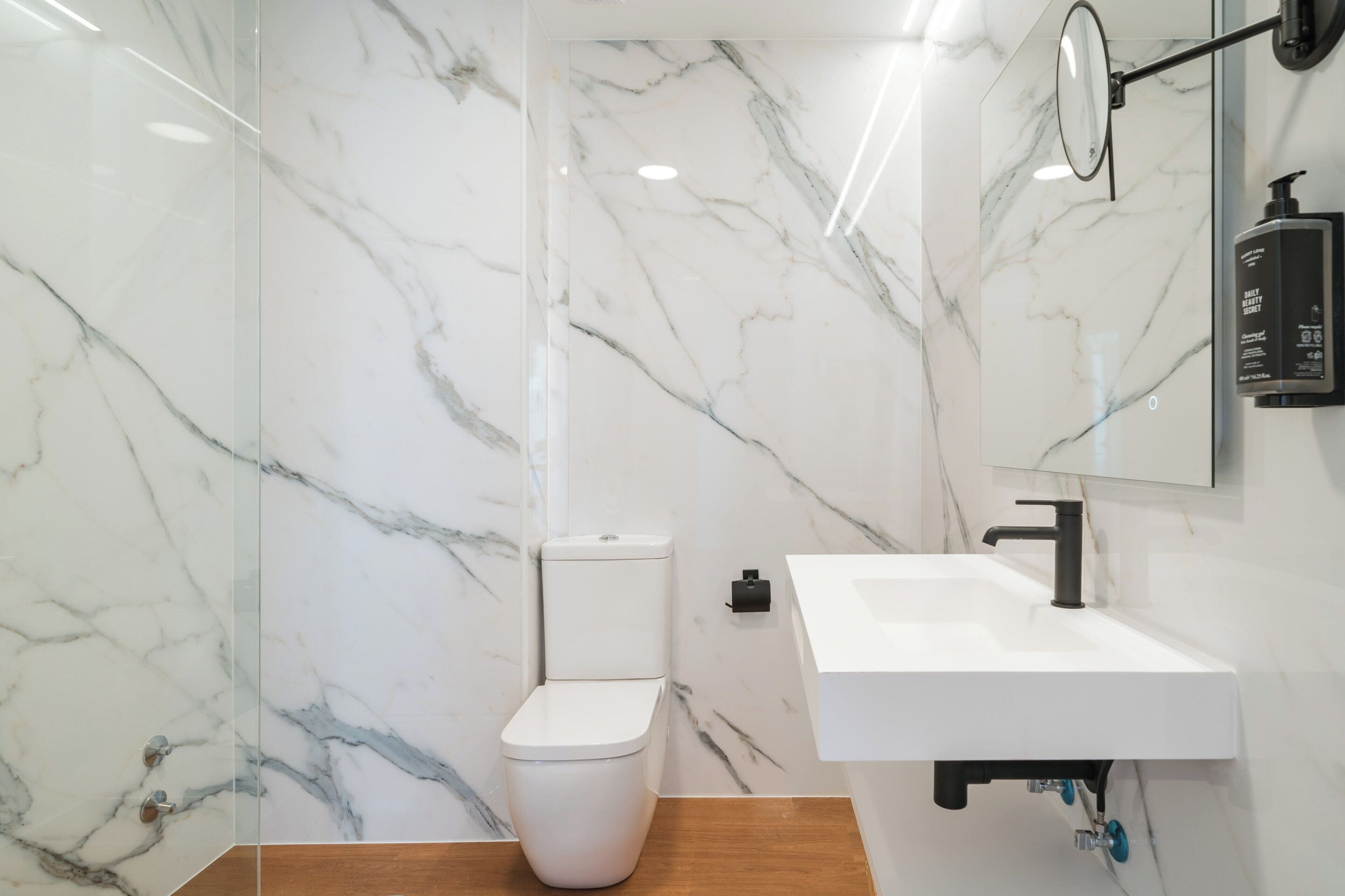 A modern bathroom with a white toilet, a white sink, and marble walls.