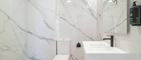 Een moderne badkamer met een wit toilet, een witte wastafel en marmeren wanden.