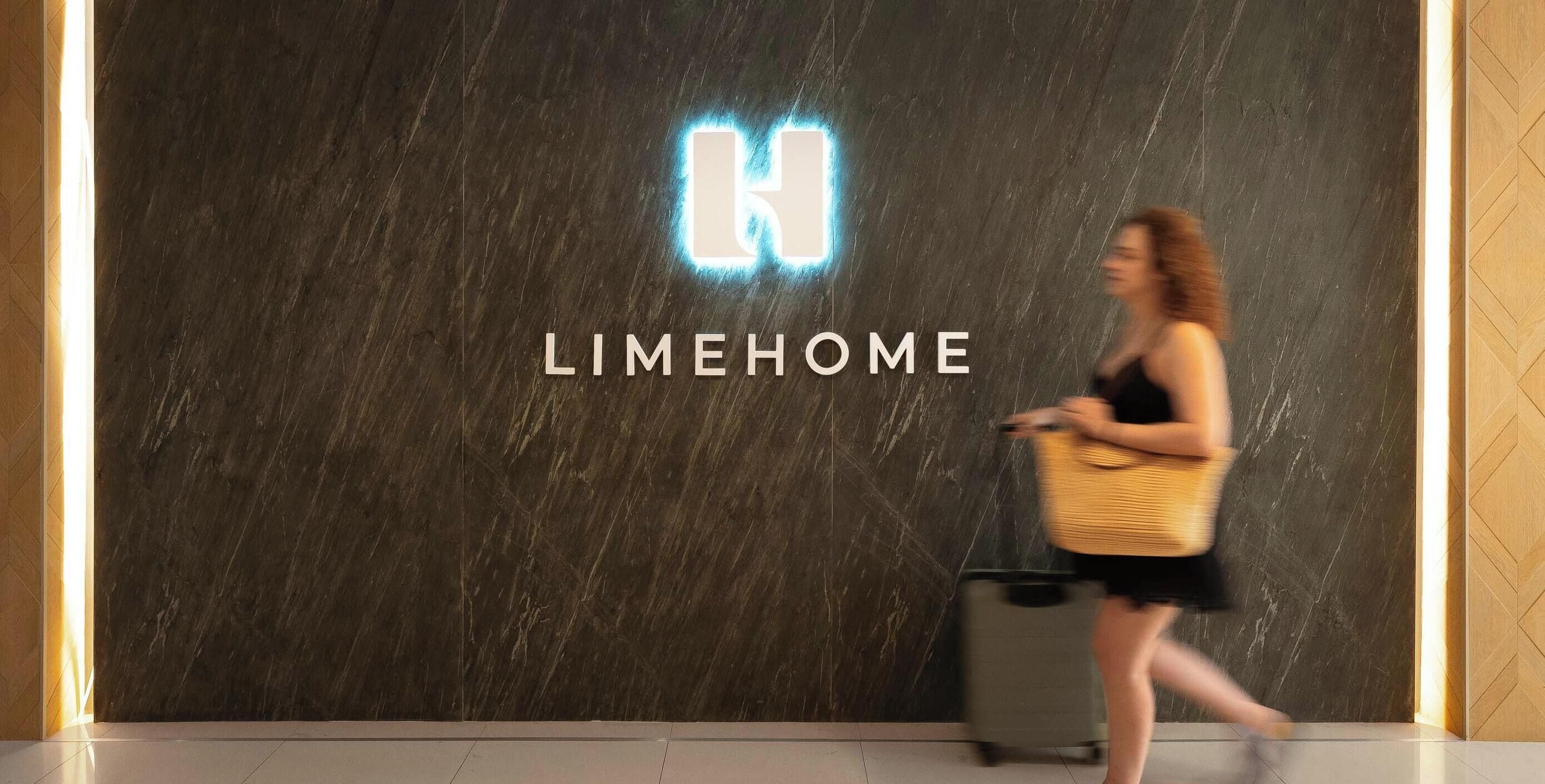 A woman walking past a wall with the word 'LIMEHOME' and a stylized 'N' logo.
