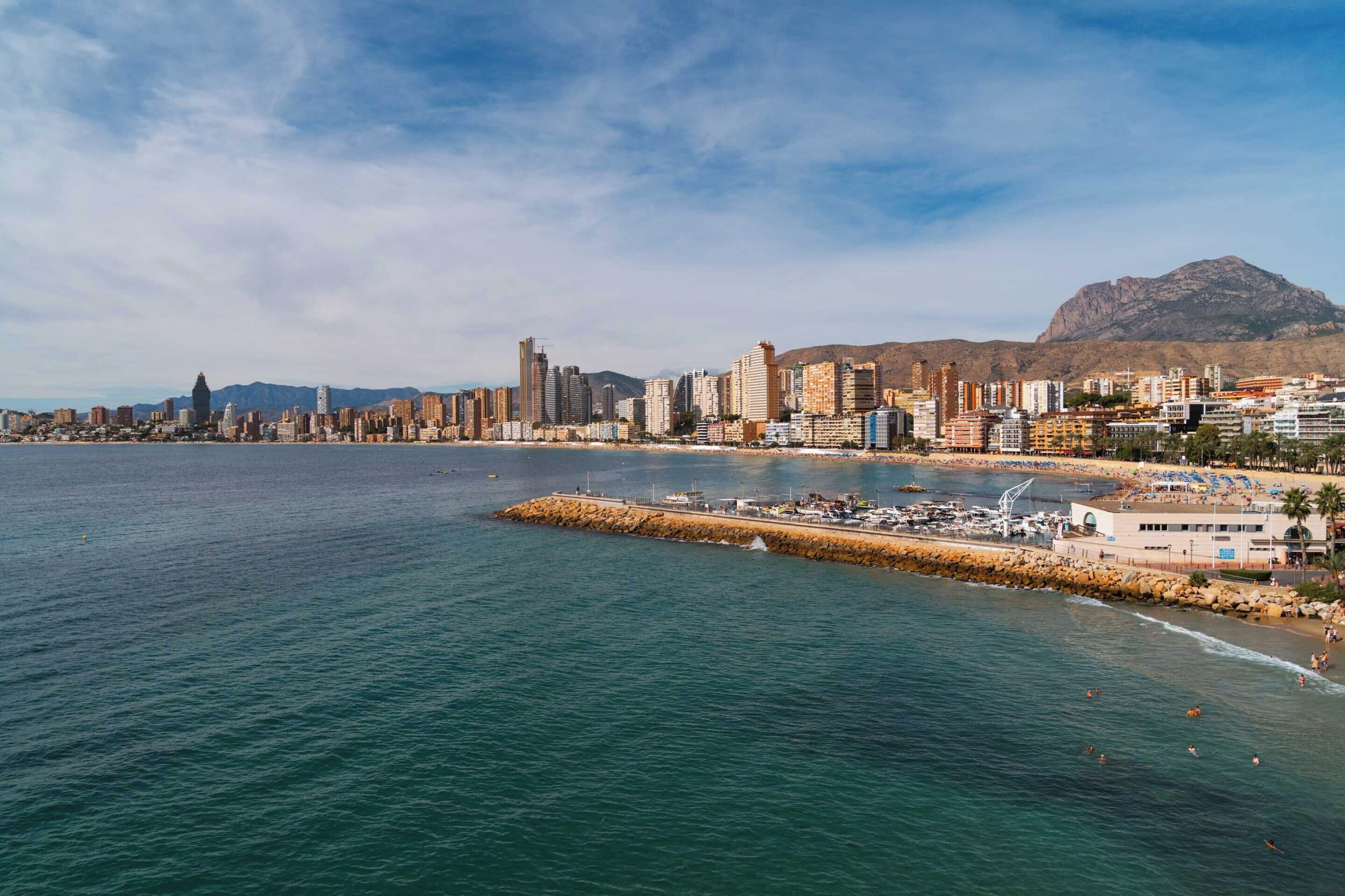 Un paysage urbain côtier avec un port de plaisance, des bâtiments et une montagne en arrière-plan.