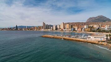 Un paisaje urbano costero con un puerto deportivo, edificios y una montaña al fondo.