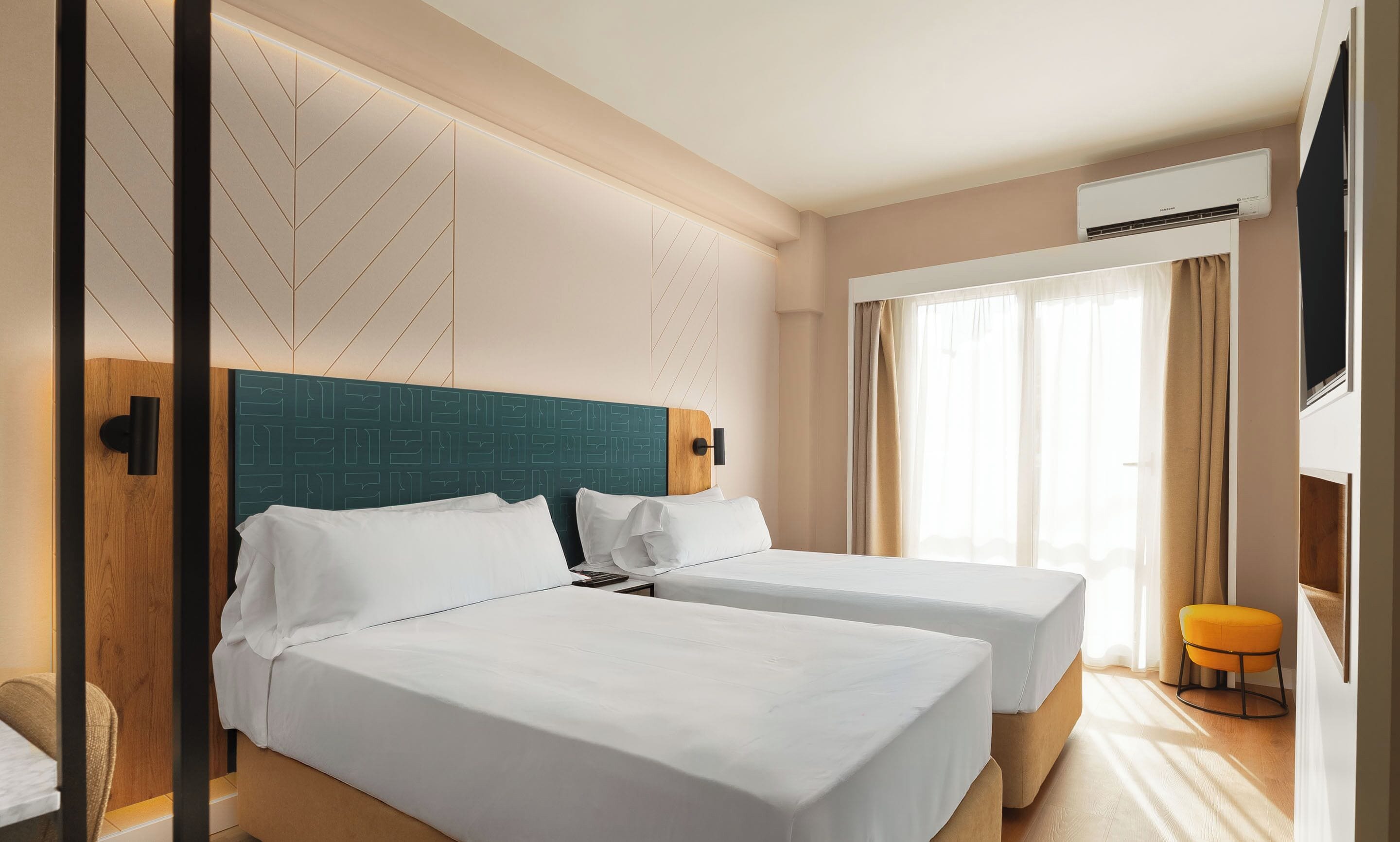 A hotel room with two beds, a large window with curtains, an air conditioning unit, and a television.