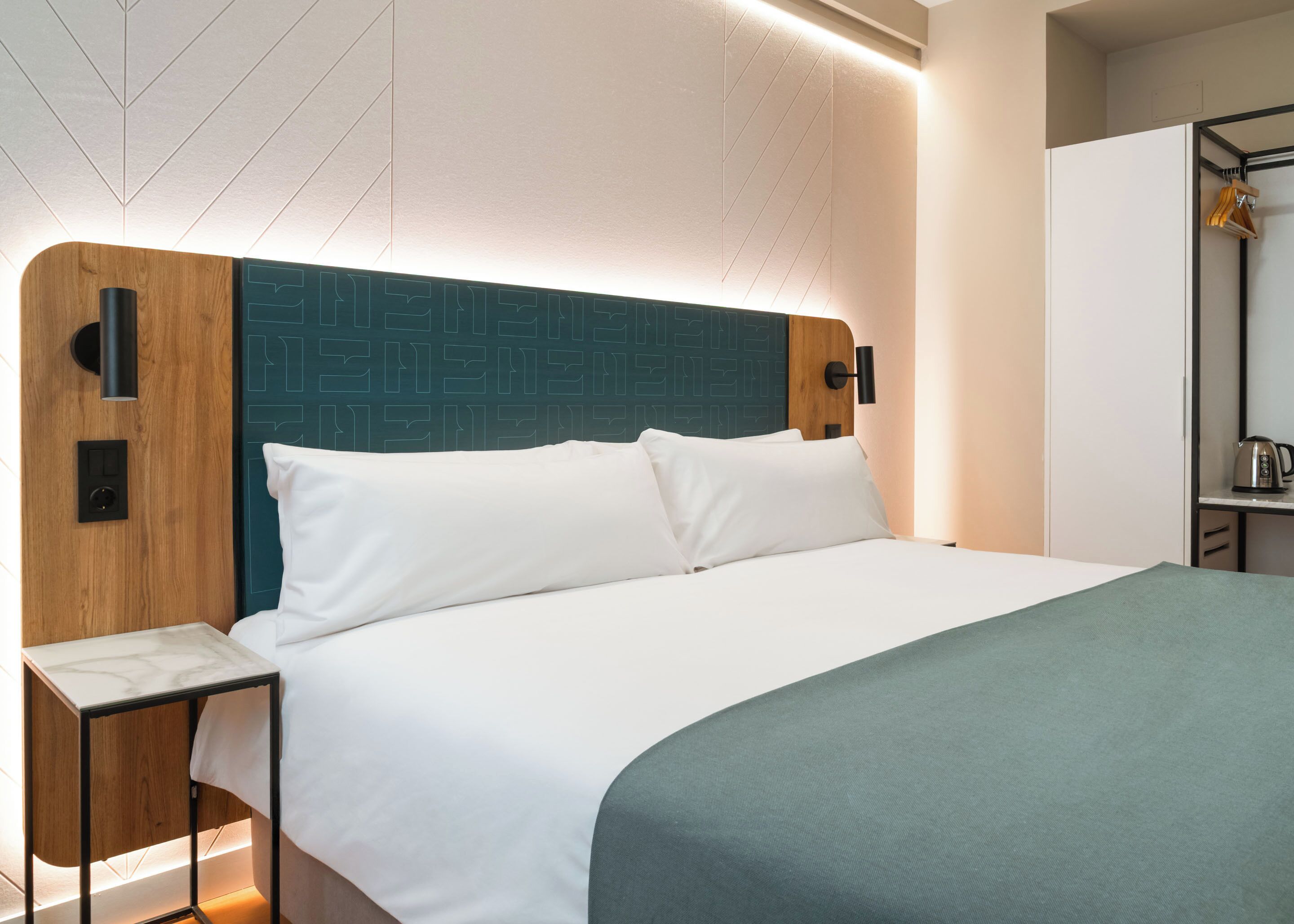 Une chambre d’hôtel moderne avec un grand lit, une tête de lit en bois, une table de chevet et une armoire.