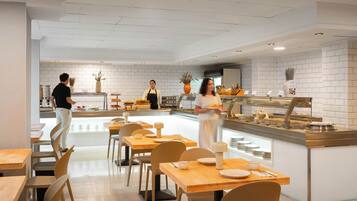 A modern cafe interior with wooden tables and chairs, a counter with food display, and a clean, white-tiled wall.