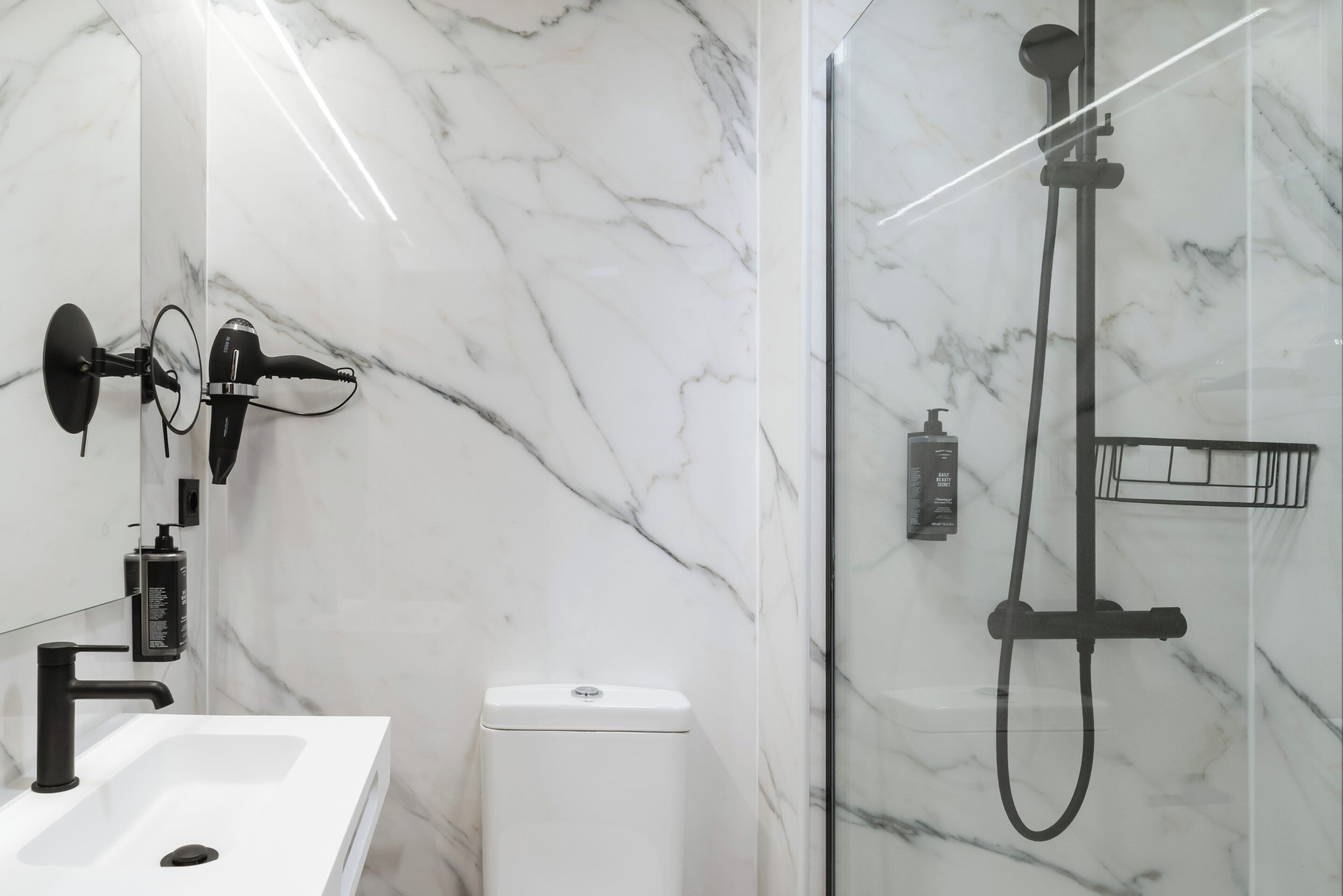 A bathroom with a white marble sink, a black handheld showerhead, and a glass-enclosed shower.