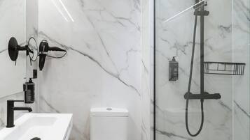 A bathroom with a white marble sink, a black handheld showerhead, and a glass-enclosed shower.