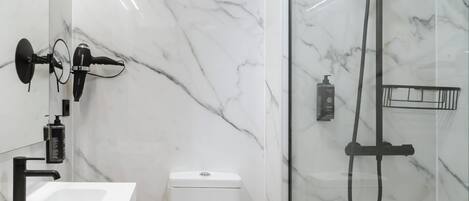 A bathroom with a white marble sink, a black handheld showerhead, and a glass-enclosed shower.