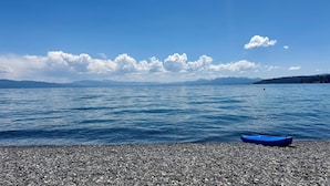 A pebbled beach with a blue boat and calm water under a clear sky.