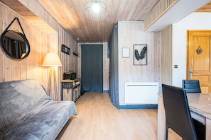 A compact room with a sofa, a dining table with chairs, a lamp, a mirror, and a door. - Apartment 'Le Gypaete Val Cenis' with Mountain View, Balcony and Wi-Fi (Termignon)