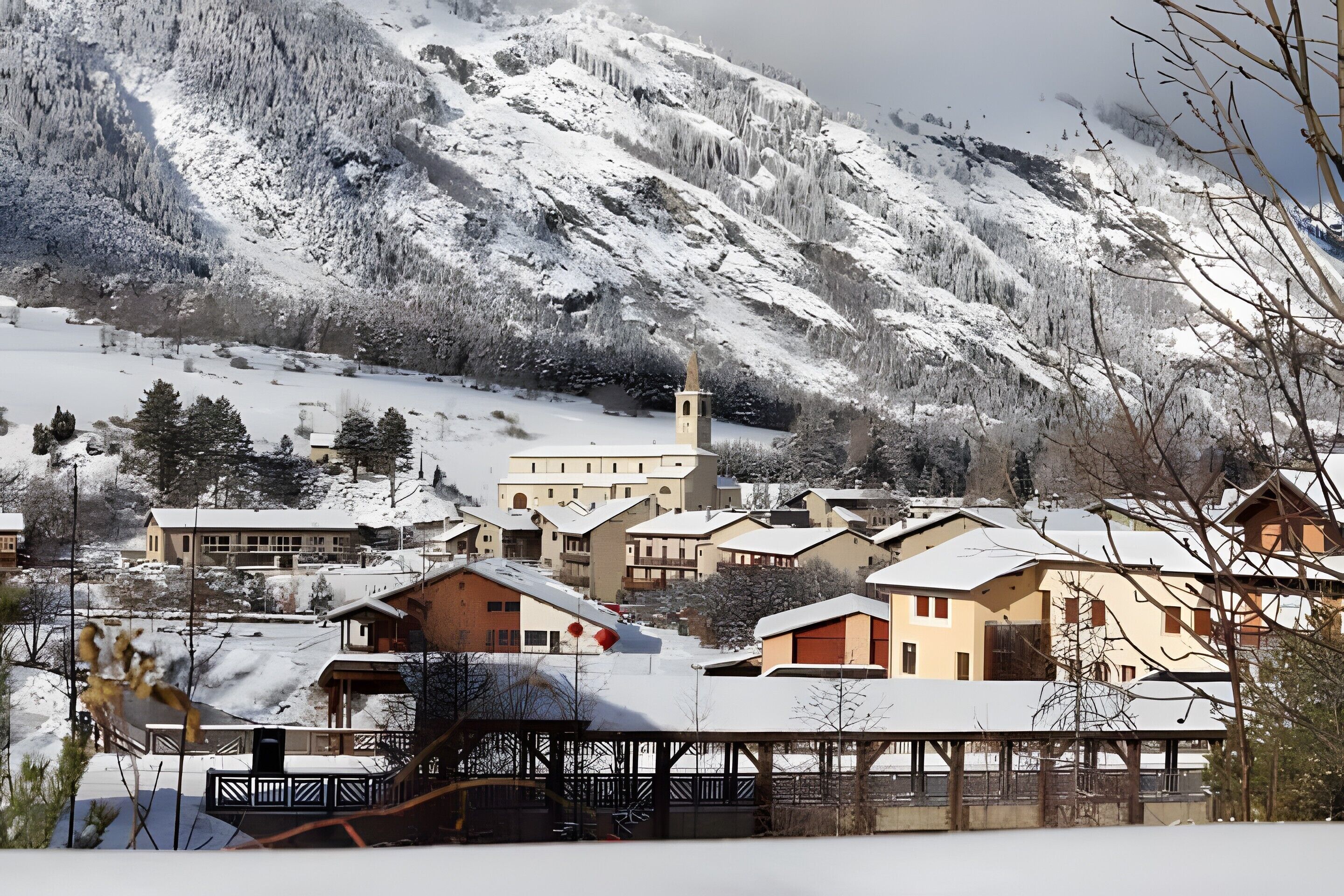 A snow-covered mountain village with traditional buildings, a church, and a ski lift.