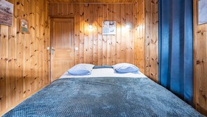 Une pièce aux murs lambrés, avec un lit, une porte et un rideau bleu.