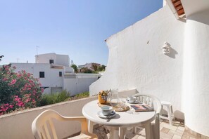 A balcony with a table set for two, a chair, a small stool, and a decorative basket.