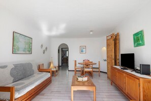 A living room with a sofa, a coffee table, a TV, and a dining area with chairs and a table.