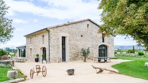 Un bâtiment en pierre doté d’un patio, d’une brouette rustique et d’un petit pot.