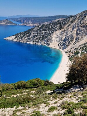 Paisagem costeira com praia, águas azul-claras e terreno rochoso.