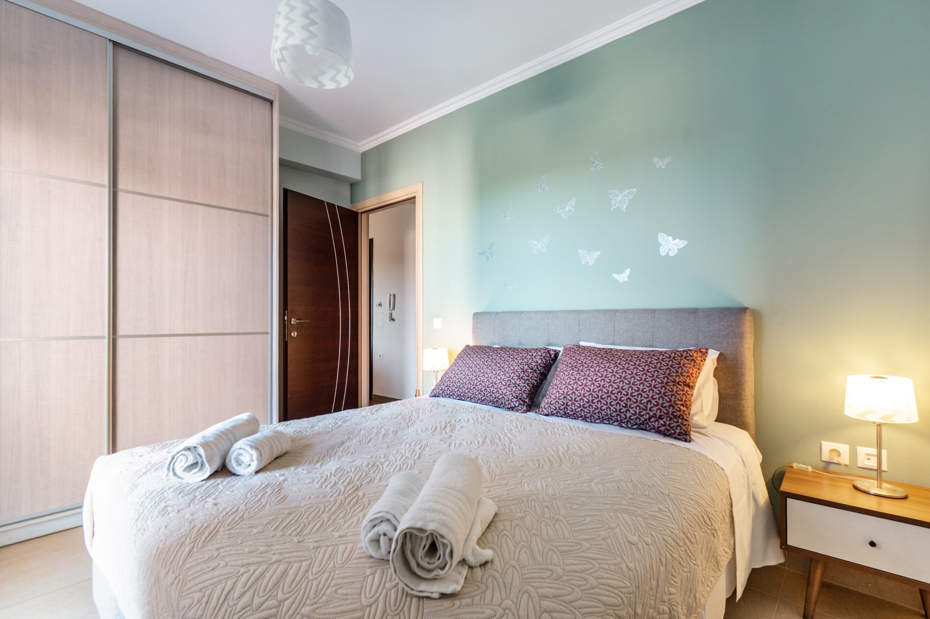 Une chambre d’hôtel avec un lit, une table de chevet, une lampe, une armoire et des autocollants représentant des papillons sur le mur.