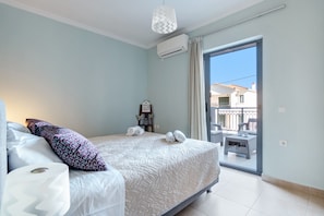 Quarto com cama, almofadas, mesa de cabeceira, aparelho de ar condicionado e vista para a varanda.